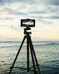 Smartphone on tripod capturing seascape sunrise. Mobile photography or videography concept.